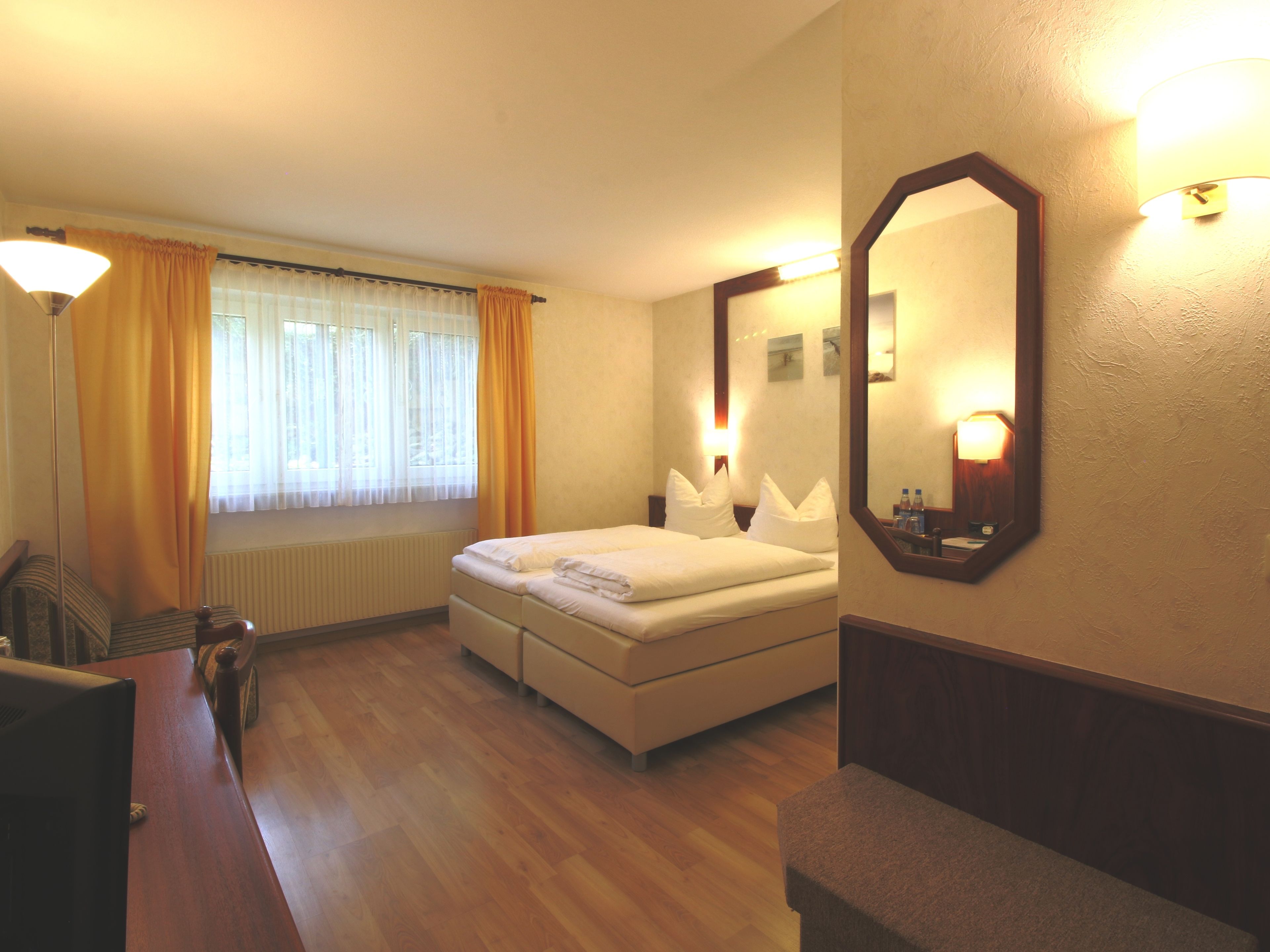 Una habitación de hotel con cama, escritorio, silla, espejo y ventana con cortinas.
