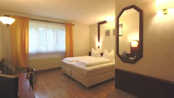 Una habitación de hotel con cama, escritorio, silla, espejo y ventana con cortinas.