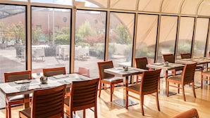 Un amplio comedor interior con grandes ventanales, mesas y sillas de madera.