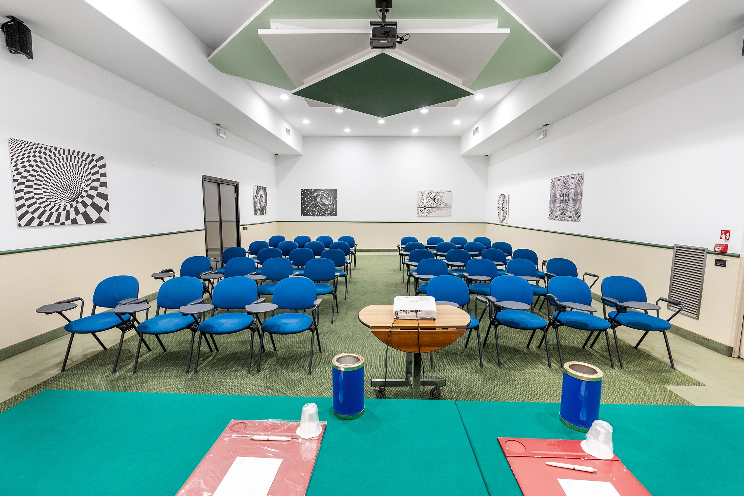 Una sala conferenze con file di sedie blu, un proiettore e una lavagna.