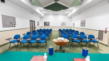 Una sala conferenze con file di sedie blu, un proiettore e una lavagna.