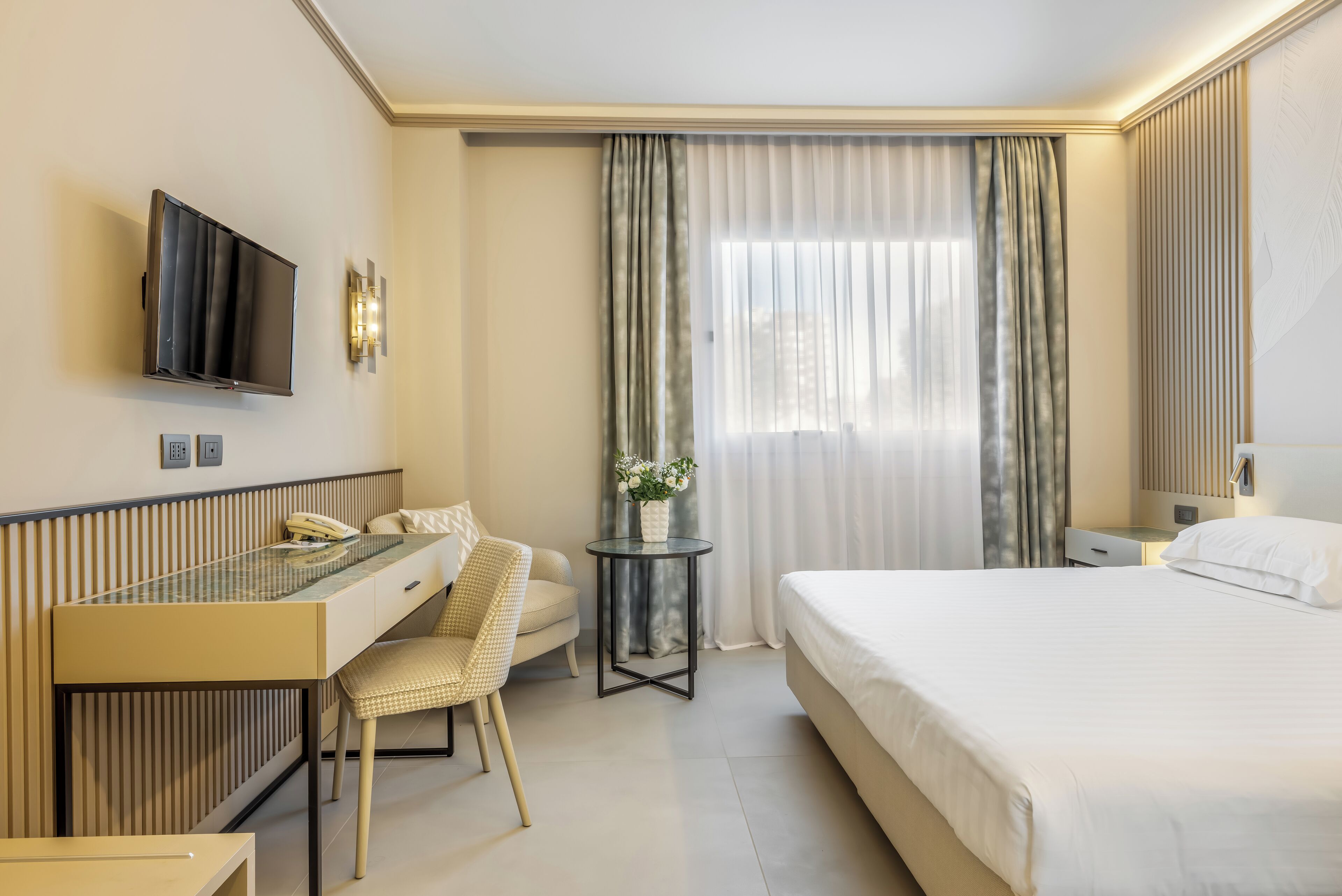 Una habitación de hotel con cama, escritorio con silla, televisor y ventana con cortinas.