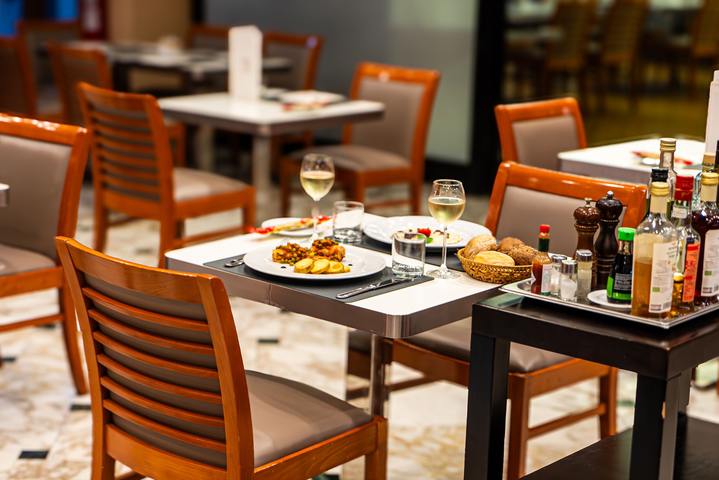 A dining area with wooden chairs and tables, plates of food, glasses of wine, and condiments.