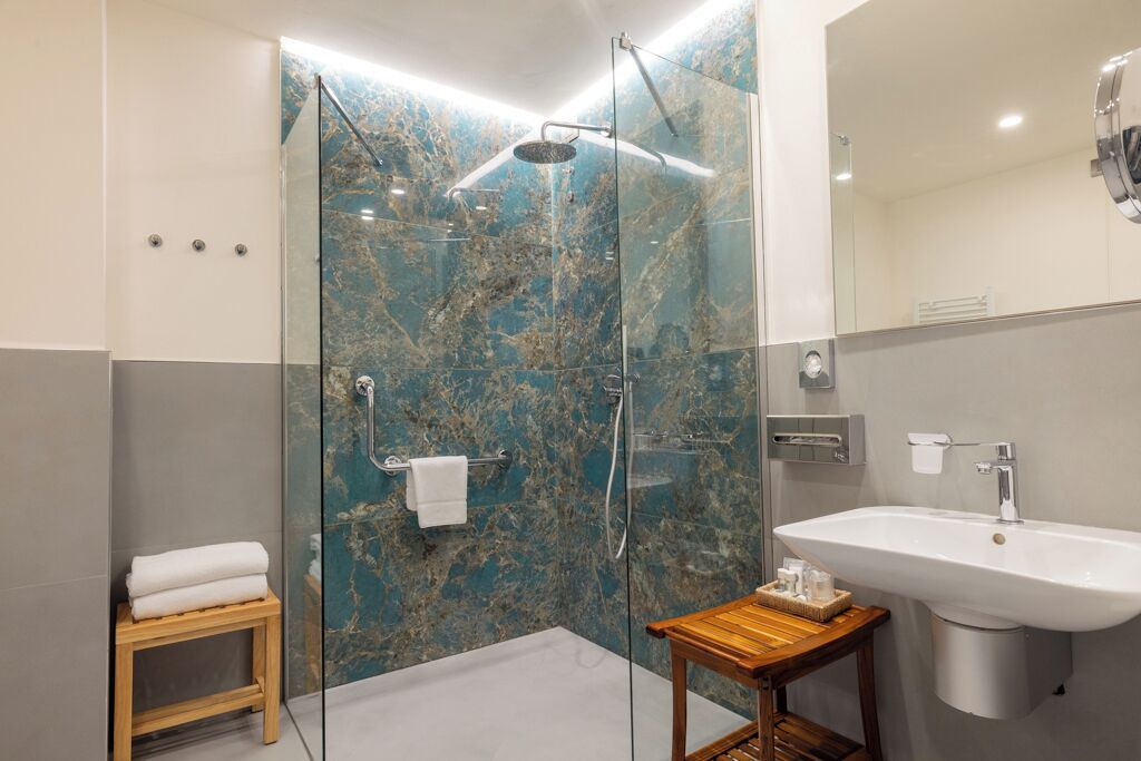Un baño moderno con ducha de vidrio, un taburete de madera, un lavabo y una pared de mármol.
