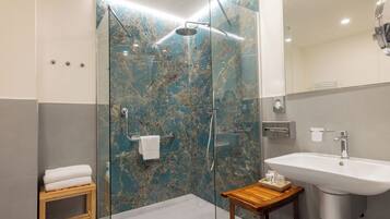 Un baño moderno con ducha de vidrio, un taburete de madera, un lavabo y una pared de mármol.