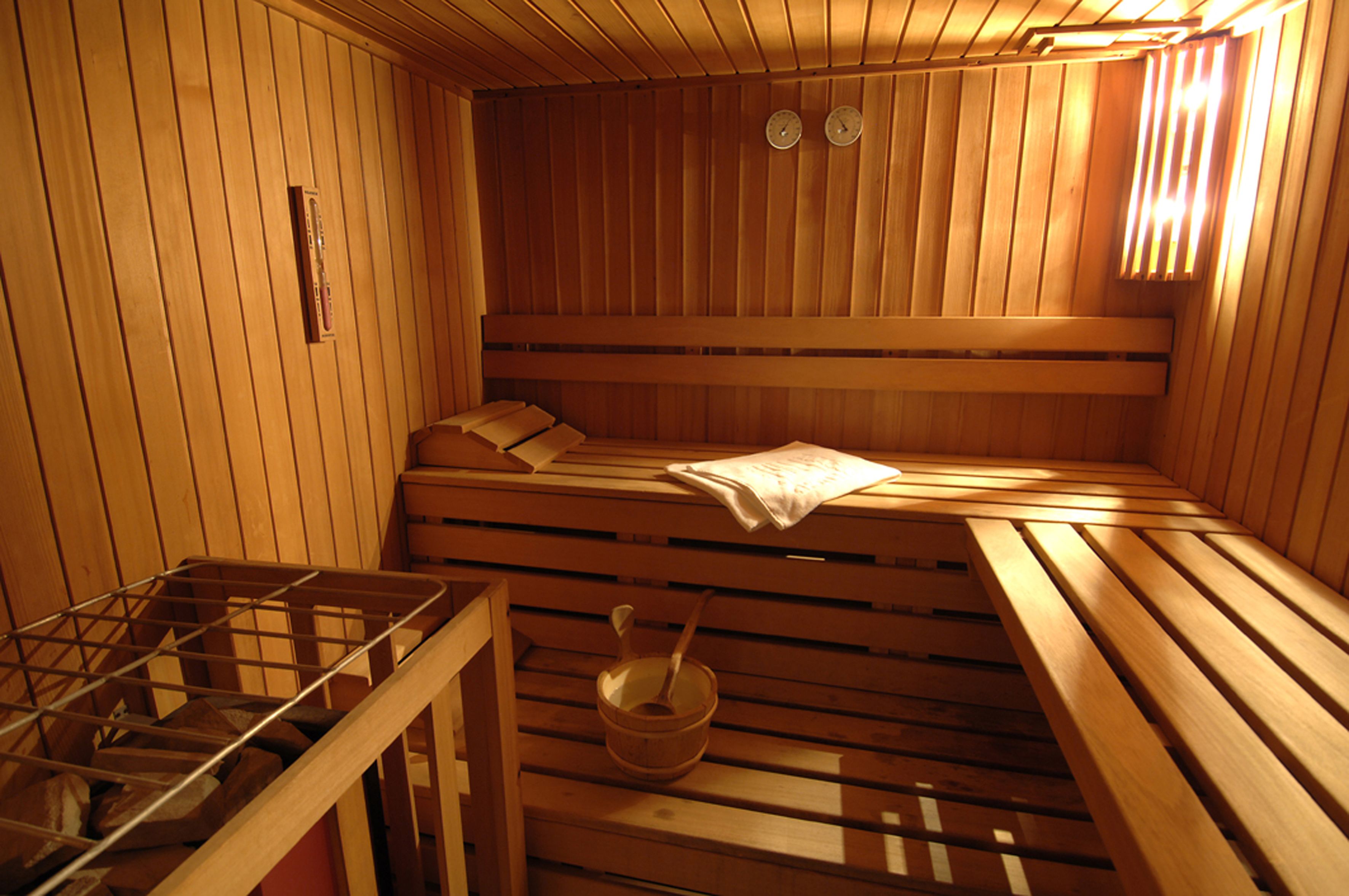 A sauna with wooden benches, a bench heater, and a wooden bucket with a ladle.