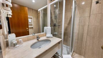 Un baño moderno con un lavabo de mármol, cabina de ducha con mampara de vidrio y un espejo grande.