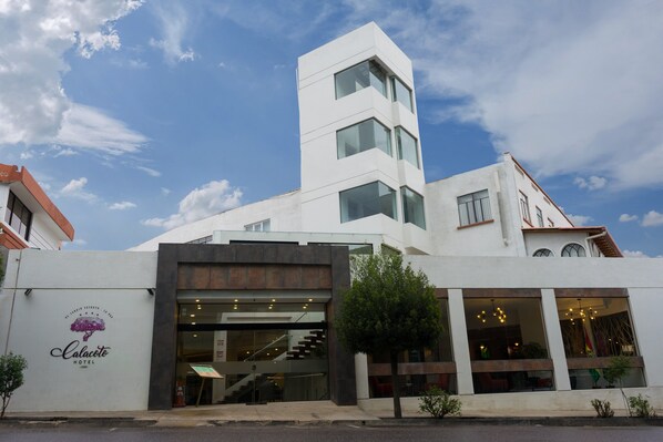Un hotel con diseño moderno, que destaca una imponente torre blanca, una escalera que conduce a la entrada y un logotipo visible en la fachada.