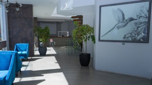 Eine moderne Lobby mit blauen Sesseln, einer großen Pflanze im Topf und einem gerahmten Kunstwerk mit einem Vogel.