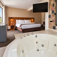 Habitación de hotel con una cama grande, un televisor en la pared, una bañera y un escritorio pequeño con una lámpara.