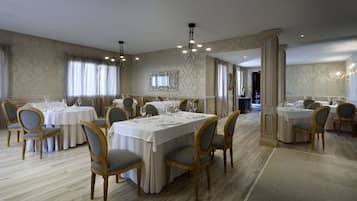 A formal dining room with multiple tables and chairs, elegant chandeliers, and a large mirror on the wall.