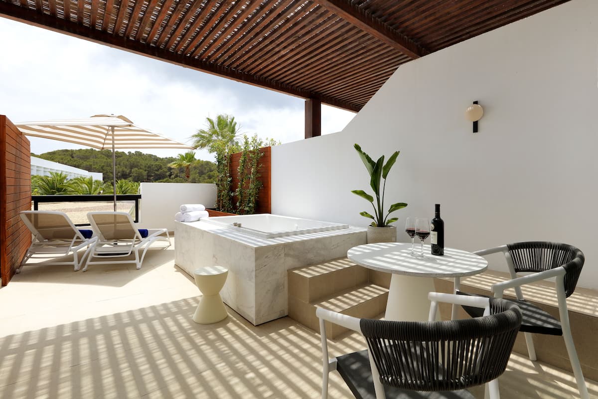 A rooftop terrace with a hot tub, lounge chairs, a table with chairs, and a pergola.