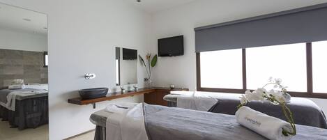 Un spa moderno con dos camillas de masaje, un espejo grande, un televisor de pantalla plana y una ventana con vistas.