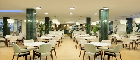 Un vaste espace dédié à la salle à manger, avec de nombreuses tables et chaises, un bar à l’arrière-plan et des piliers recouverts de carreaux verts.