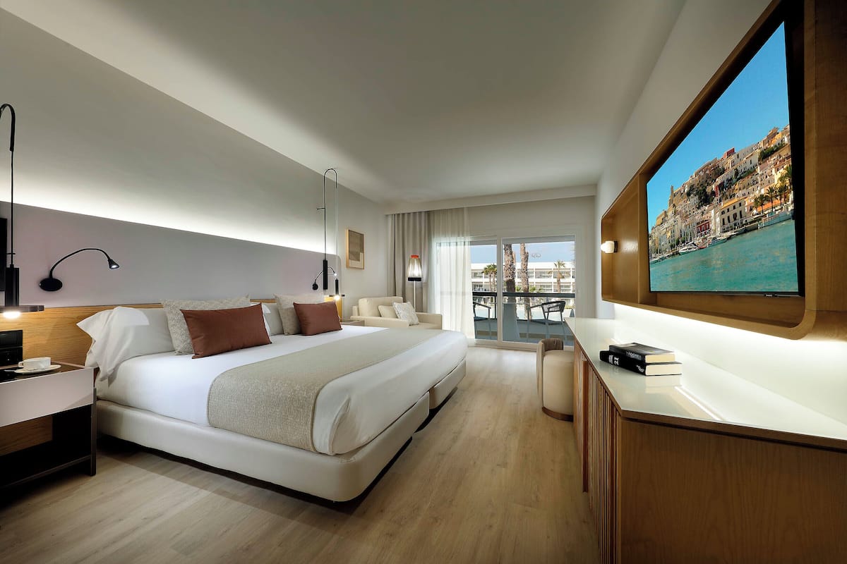 A modern hotel room with a large bed, bedside tables, a desk, and a large window with a city view.