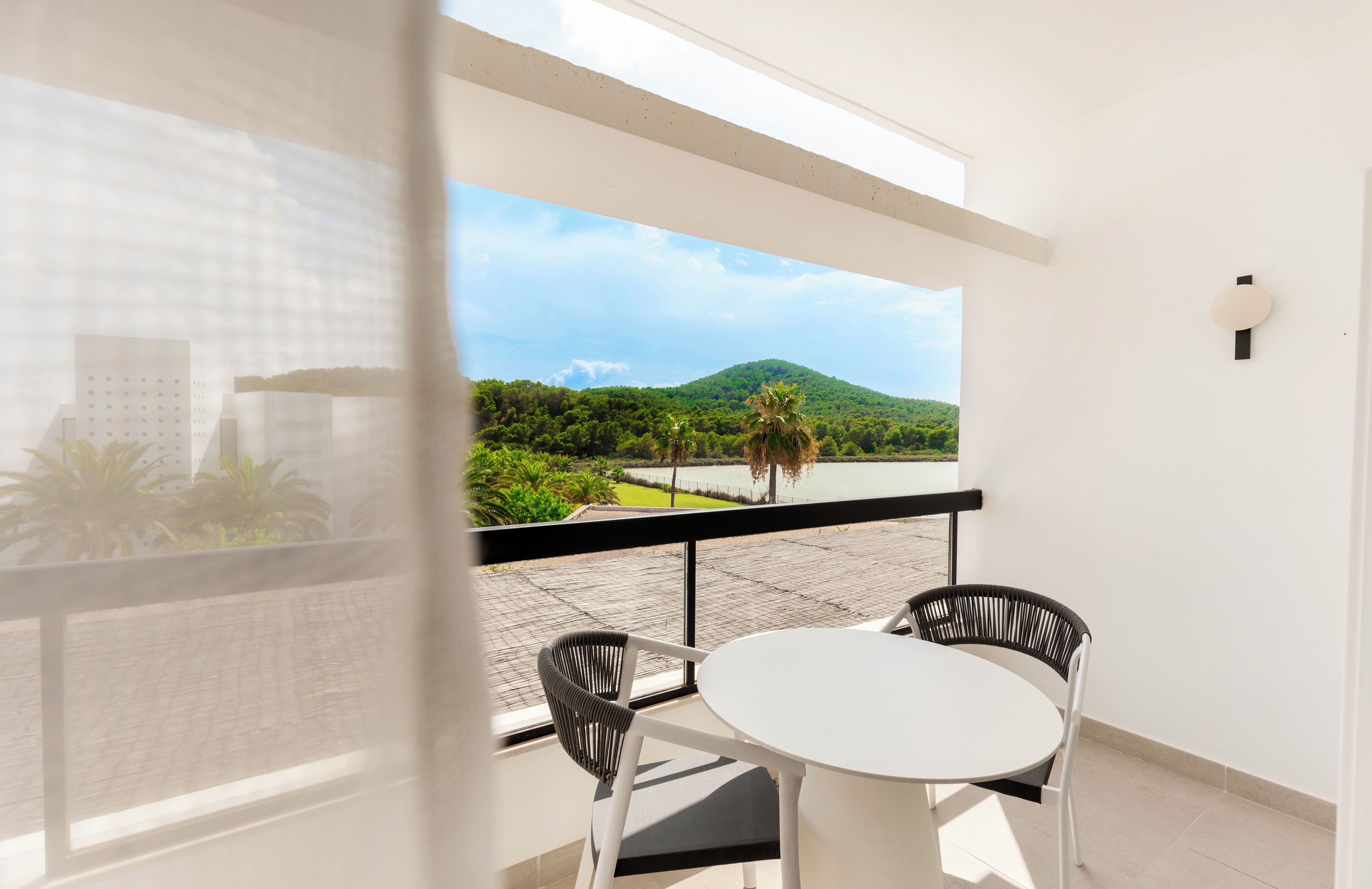 Un balcon avec une table blanche et deux chaises, donnant sur un paysage verdoyant et luxuriant, avec une colline et des palmiers.