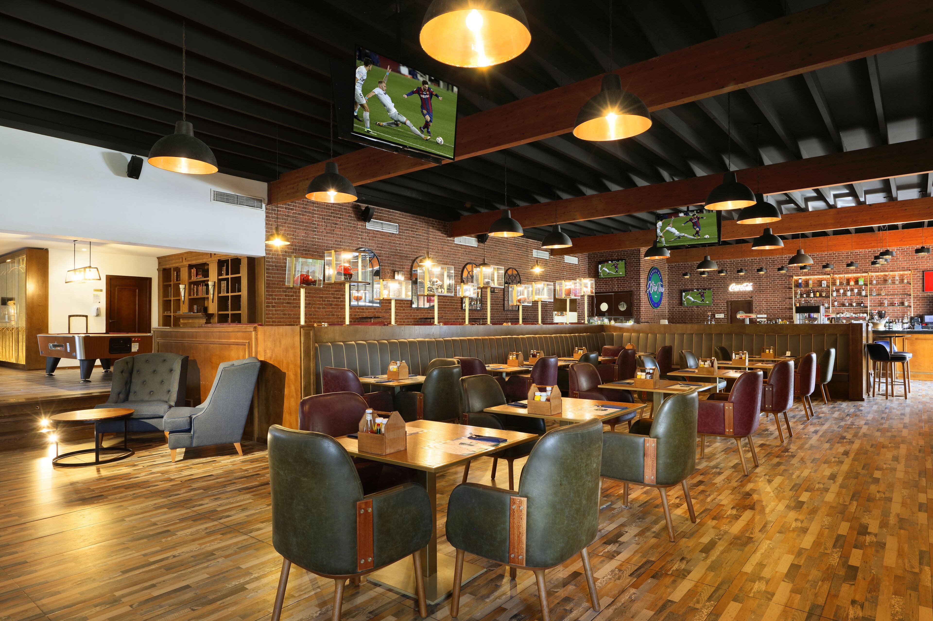Ein Restaurant mit Holzboden, mehreren Tischen und Stühlen, hängenden Lampen und einer Ziegelwand.