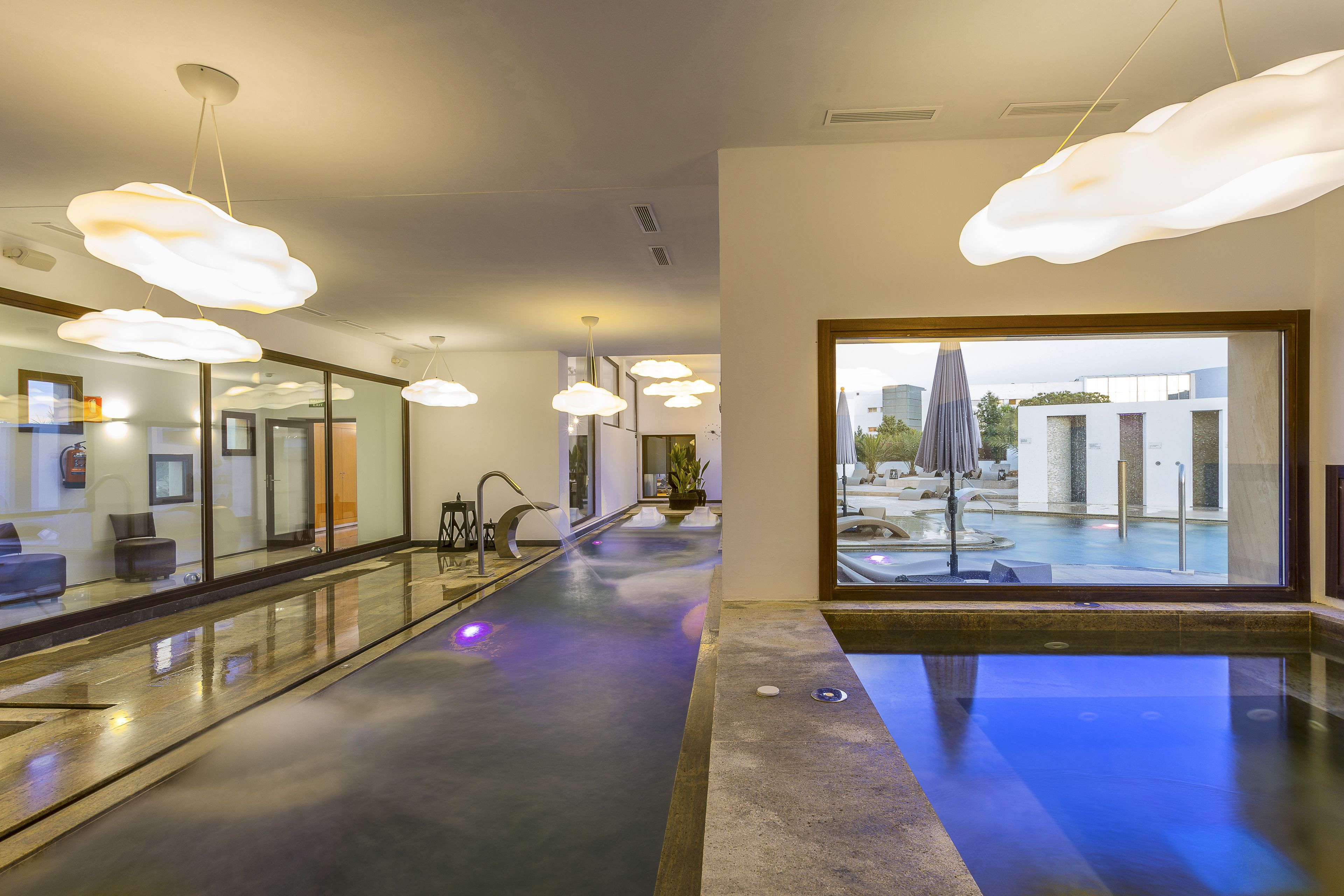 Un moderno vestíbulo de hotel con piscina de cristal, iluminación contemporánea y vistas al exterior.