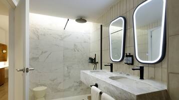 Un baño moderno con ducha de mármol, lavamanos doble y un espejo grande con iluminación integrada.