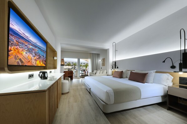 Una habitación de hotel moderna con una cama grande, un escritorio con cafetera, un televisor montado en la pared y vistas a la ciudad desde la ventana.