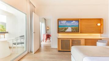 A modern hotel room with a glass door leading to a balcony, a wooden bedside table, a bed, and a wall-mounted TV displaying a scenic view.