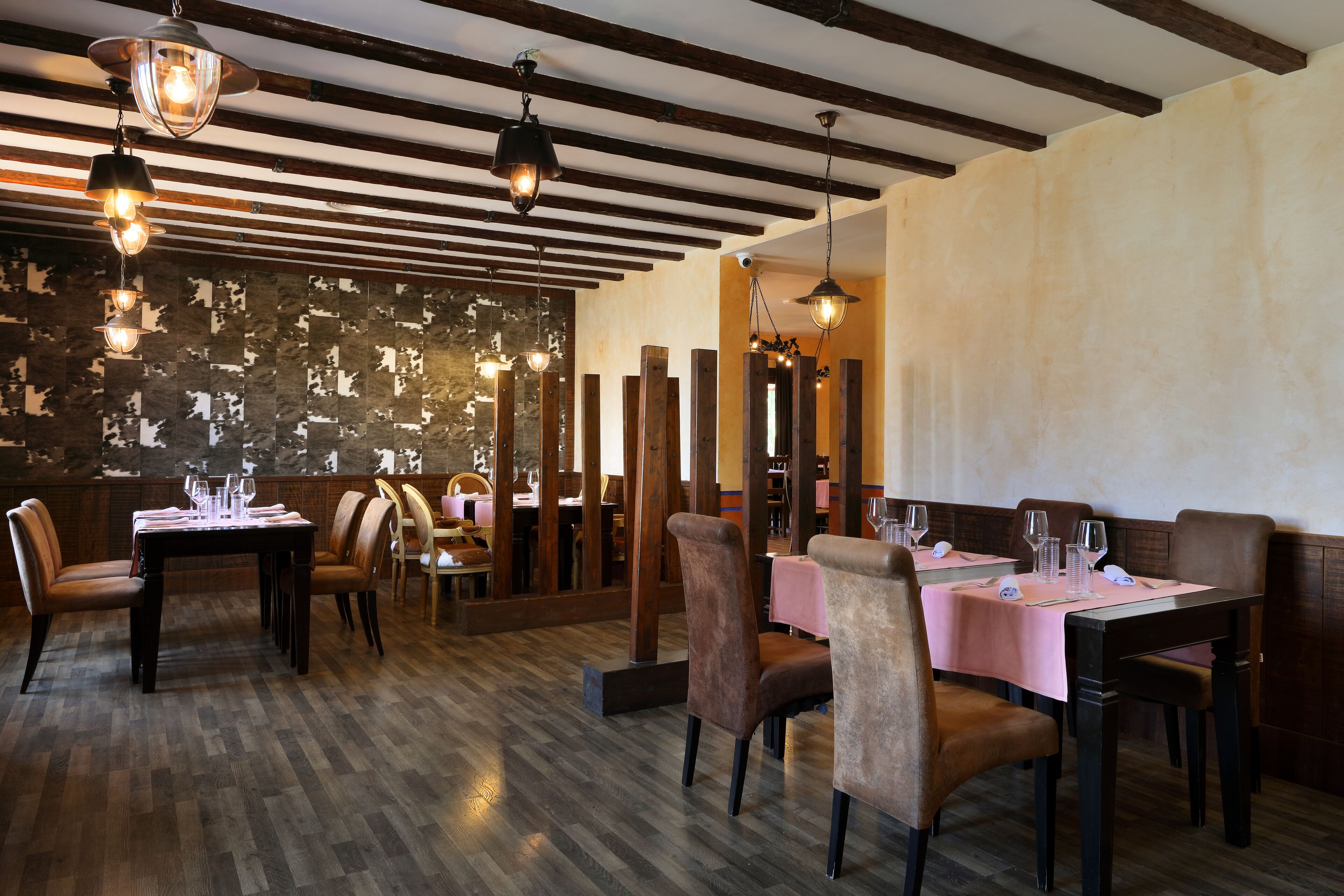 A restaurant with wooden beams, a patterned wall, and tables set for dining.