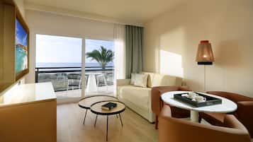 A modern hotel room with a balcony, a sofa, a coffee table, and a desk.