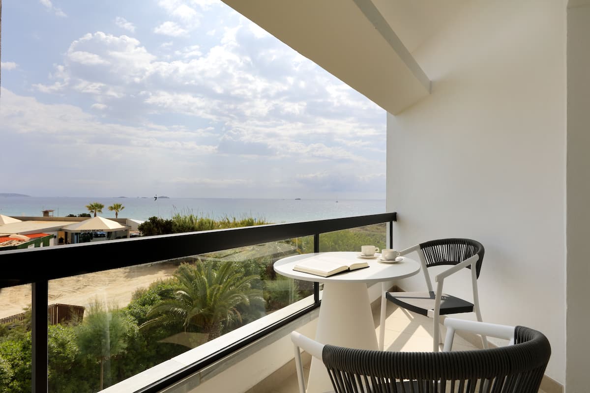 A balcony with a view of the sea, a round table with chairs, and a book.