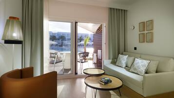 A modern living room with a sofa, two side tables, a lamp, and a view of an outdoor deck with chairs and umbrellas.