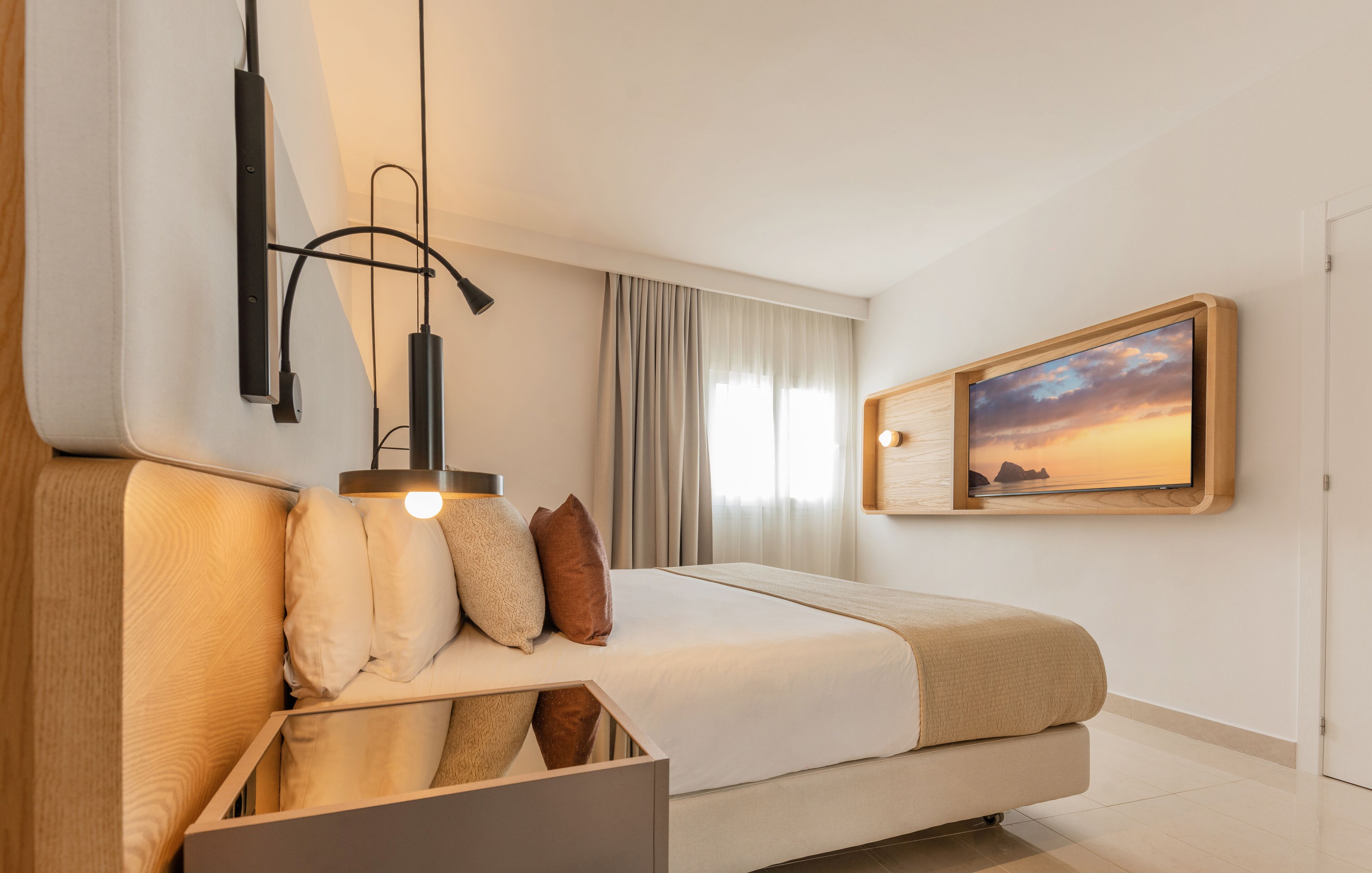 Une chambre d’hôtel moderne, équipée d’un lit, d’un bureau et d’un tableau représentant un coucher de soleil.