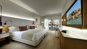 Una habitación de hotel moderna con una cama grande, mesitas de noche, un escritorio y un ventanal con vistas a la ciudad.
