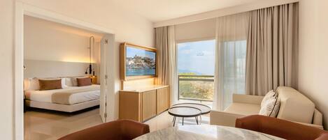 A hotel room with a bed, a seating area with a table, a television mounted on the wall, and a large window with curtains.