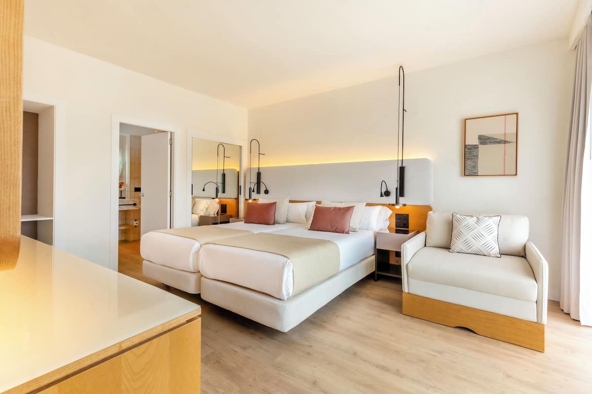A modern hotel room with a double bed, a sofa, a desk, and a mirror.