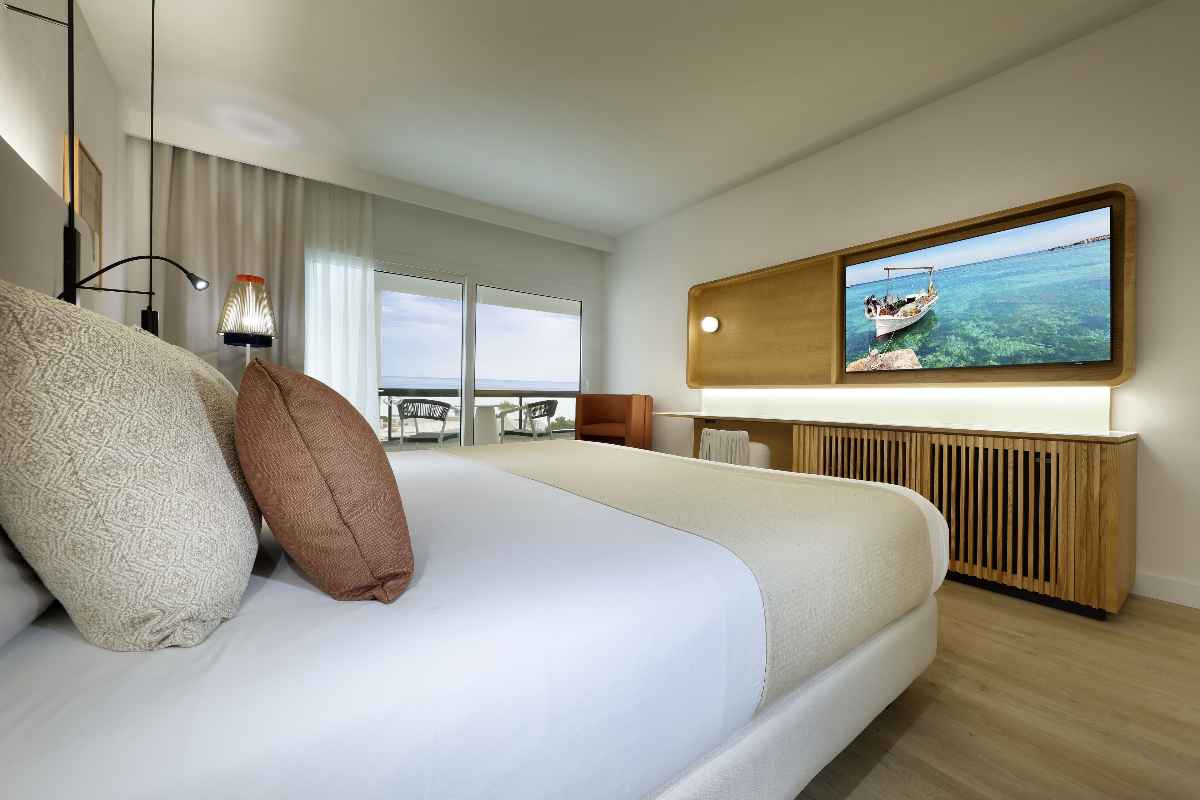 Habitación de hotel moderna con una cama grande, un televisor montado en la pared y vistas al mar a través de la ventana.