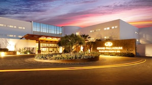 Una entrada de hotel moderna con jardín ajardinado, cielo despejado y atardecer.
