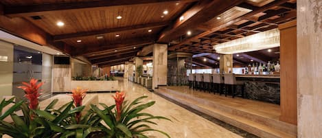 Un vestíbulo amplio con techo de madera, zona de bar con taburetes y mostrador de recepción.