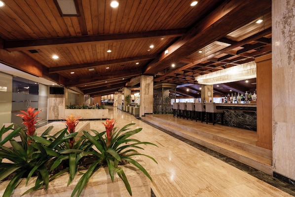 Un vestíbulo amplio con techo de madera, zona de bar con taburetes y mostrador de recepción.