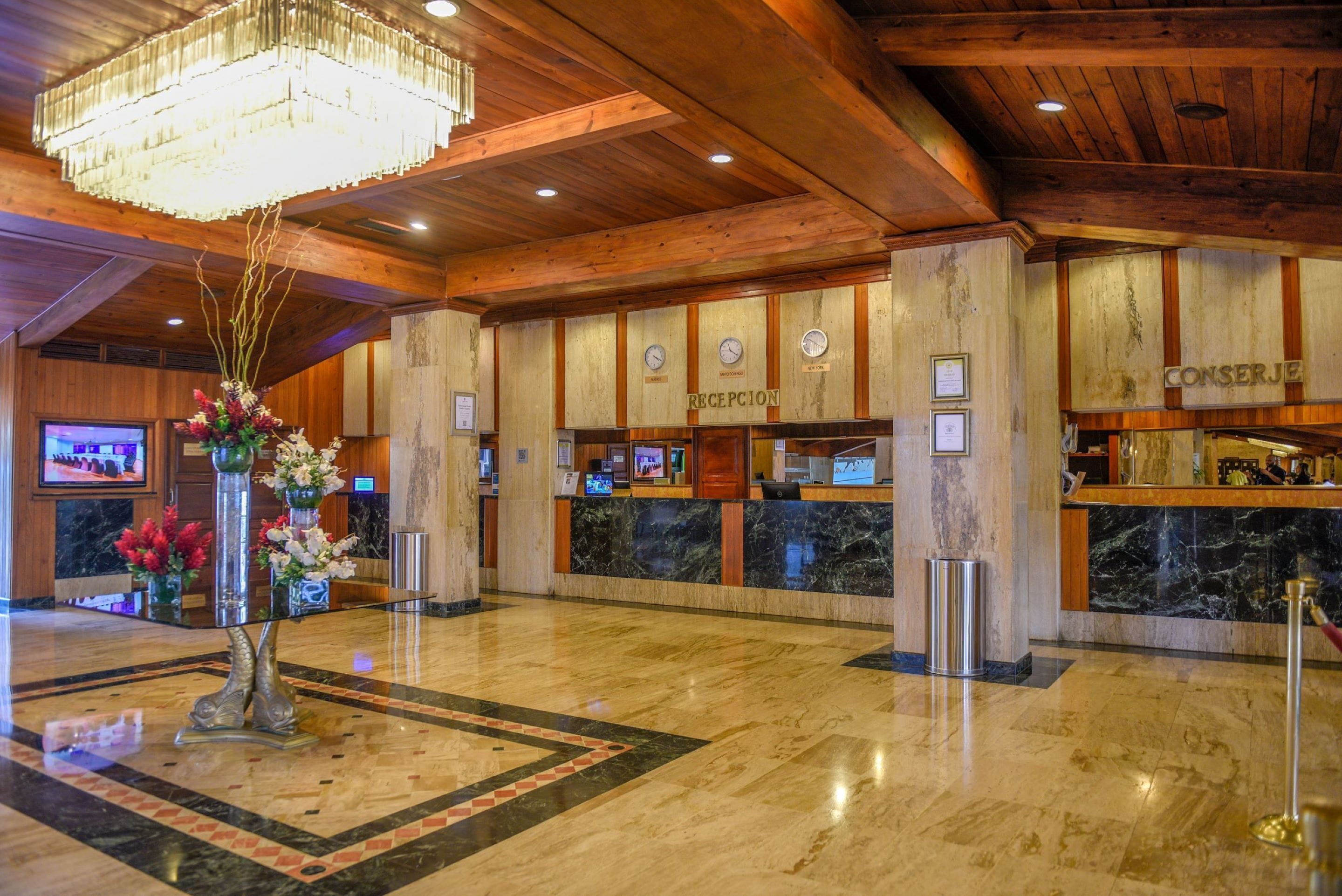 A lobby with a reception desk, a chandelier, and a floral arrangement.