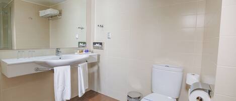 A bathroom with a sink, mirror, toilet, and a trash can.