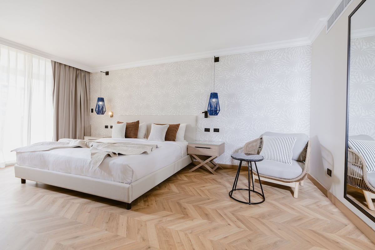 A modern hotel room with a large bed, a small side table, a chair, and a large mirror.