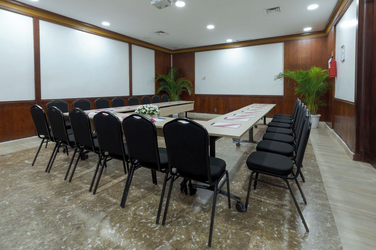 A conference room with a long table, black chairs, and a projector screen.