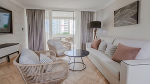 A modern living room with a sofa, wicker chairs, a round coffee table, and a large window with curtains.
