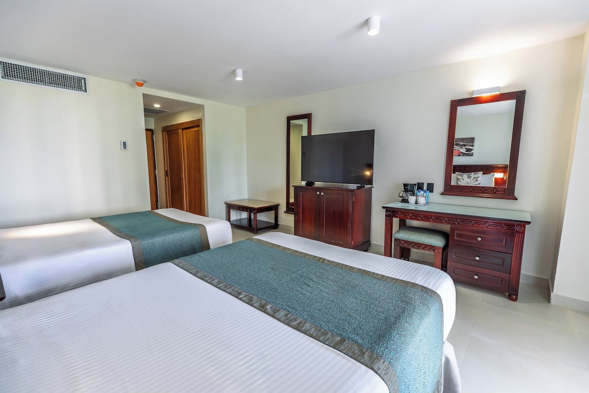 A hotel room with two beds, a desk with a mirror, a television, and a small table.