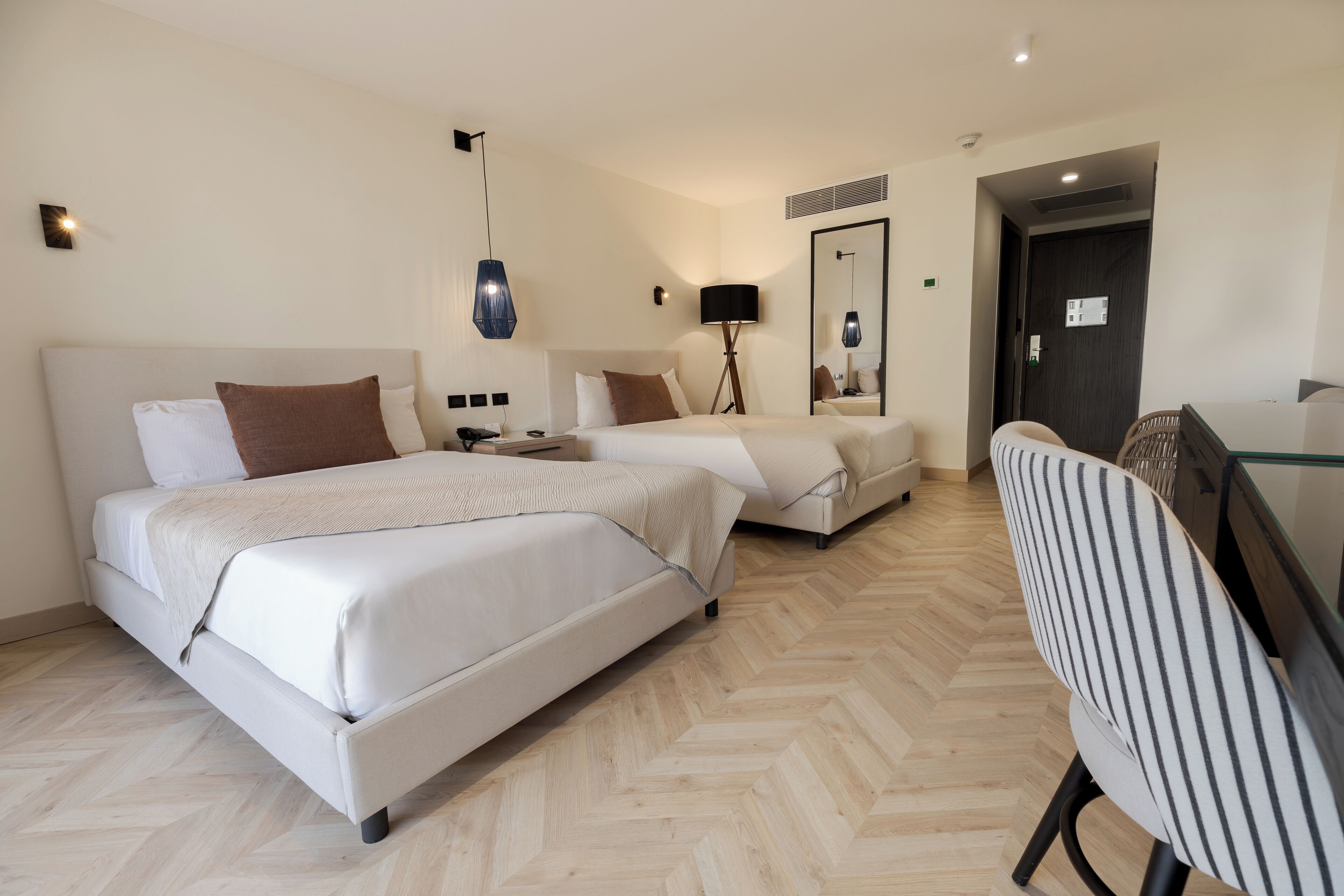 Una habitación de hotel con dos camas, un escritorio, una silla, una lámpara y un espejo.