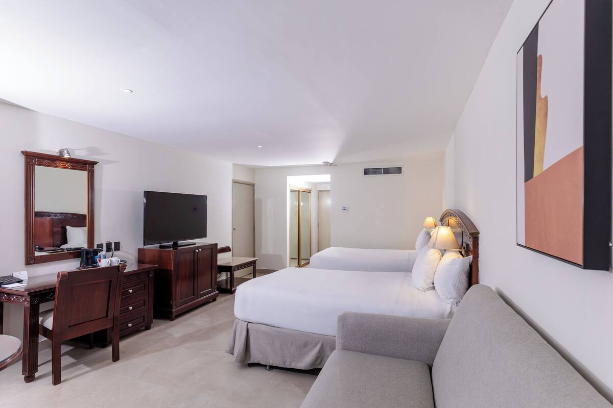 A hotel room with a bed, a sofa, a desk, a TV, and a mirror.