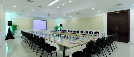 Un salón de conferencias con una larga mesa, sillas, una pantalla de proyector y una puerta con la etiqueta 'SALIDA'.