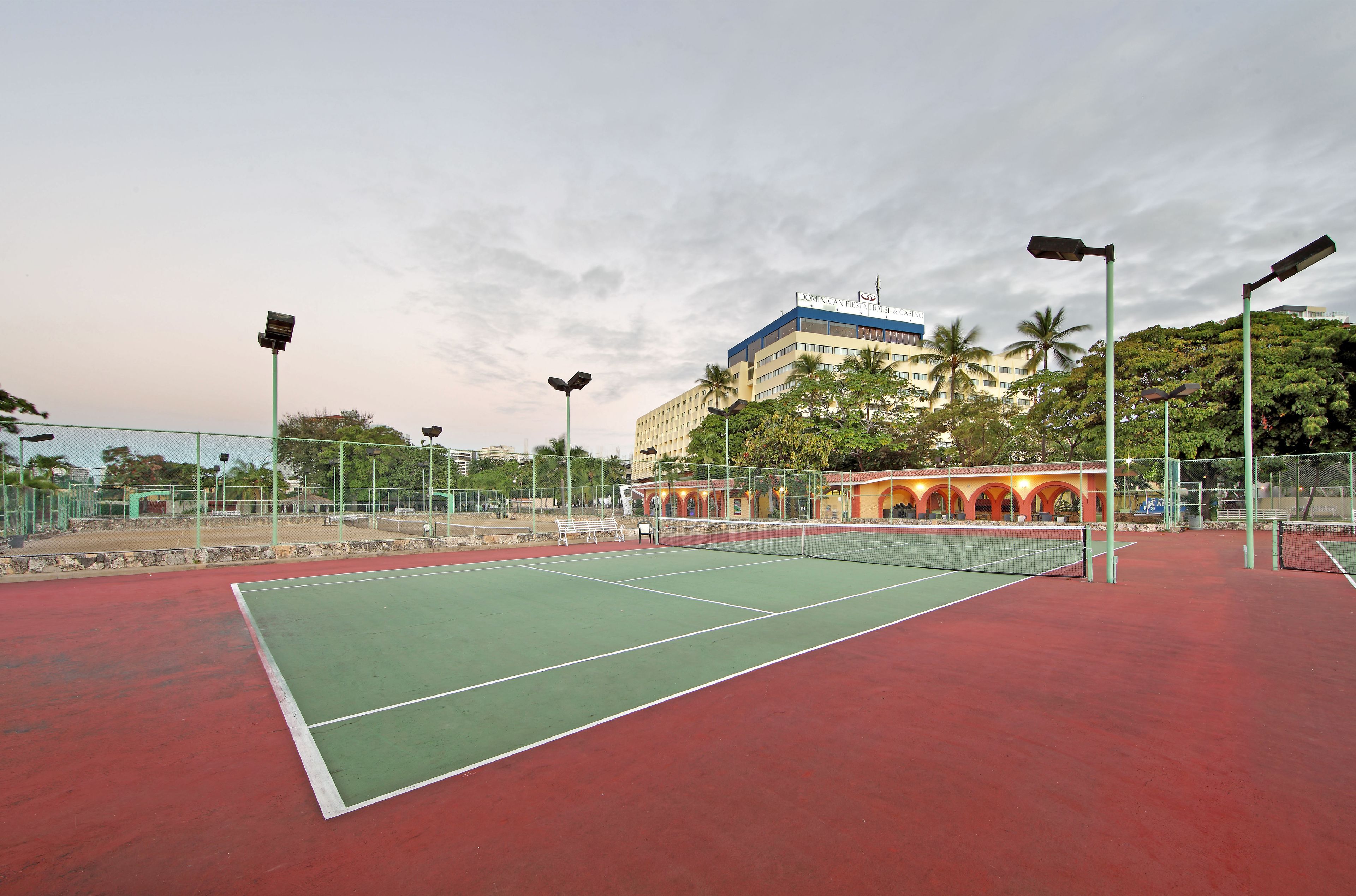 A tennis court with a net, surrounded by a fence and street lamps.