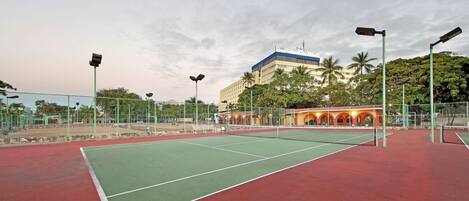 A tennis court with a net, surrounded by a fence and street lamps.