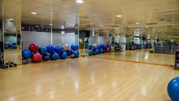 Un gimnasio amplio con pisos de madera, pelotas de ejercicio y espejos.