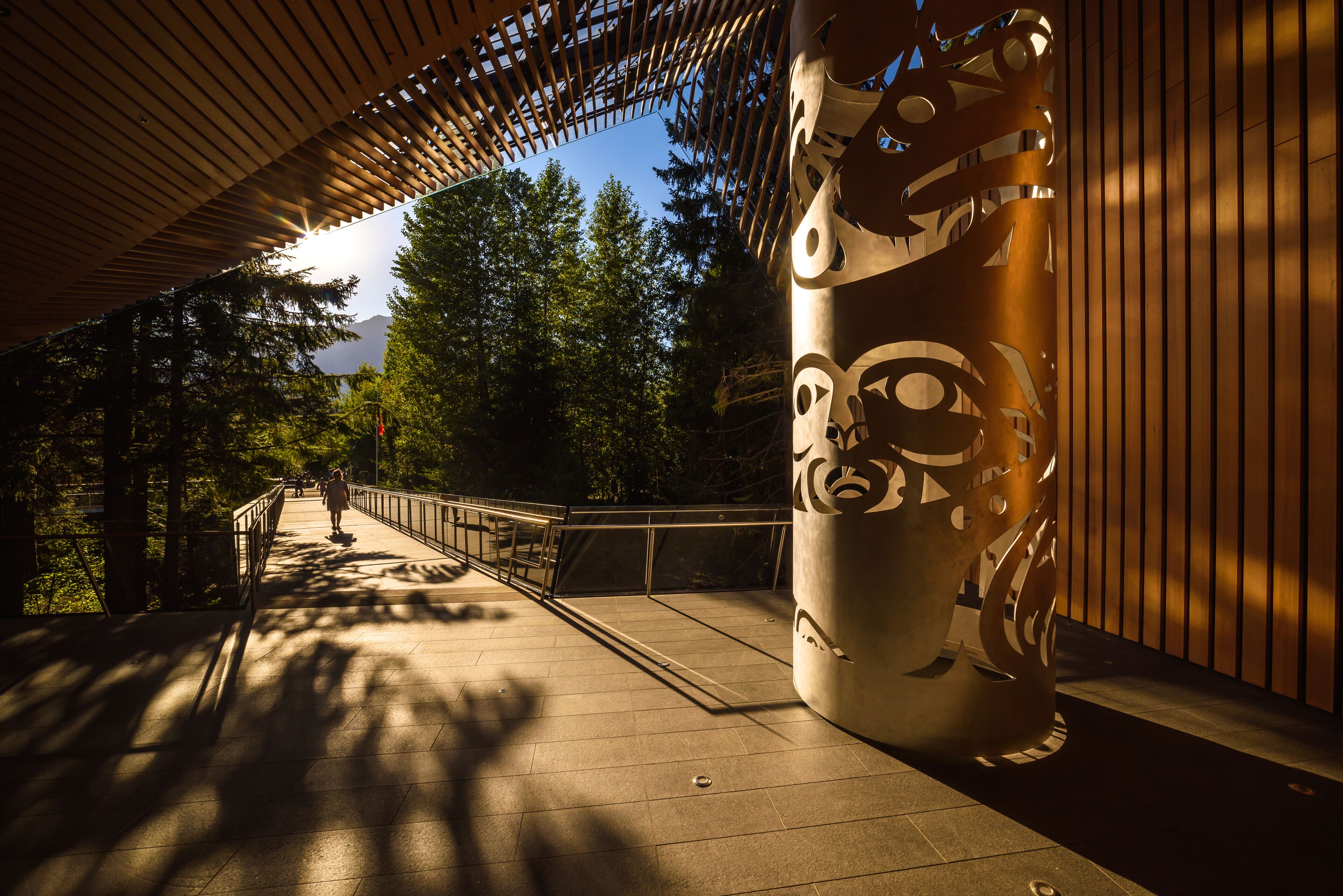 A covered walkway with a metal sculpture, a railing, and trees in the background.
